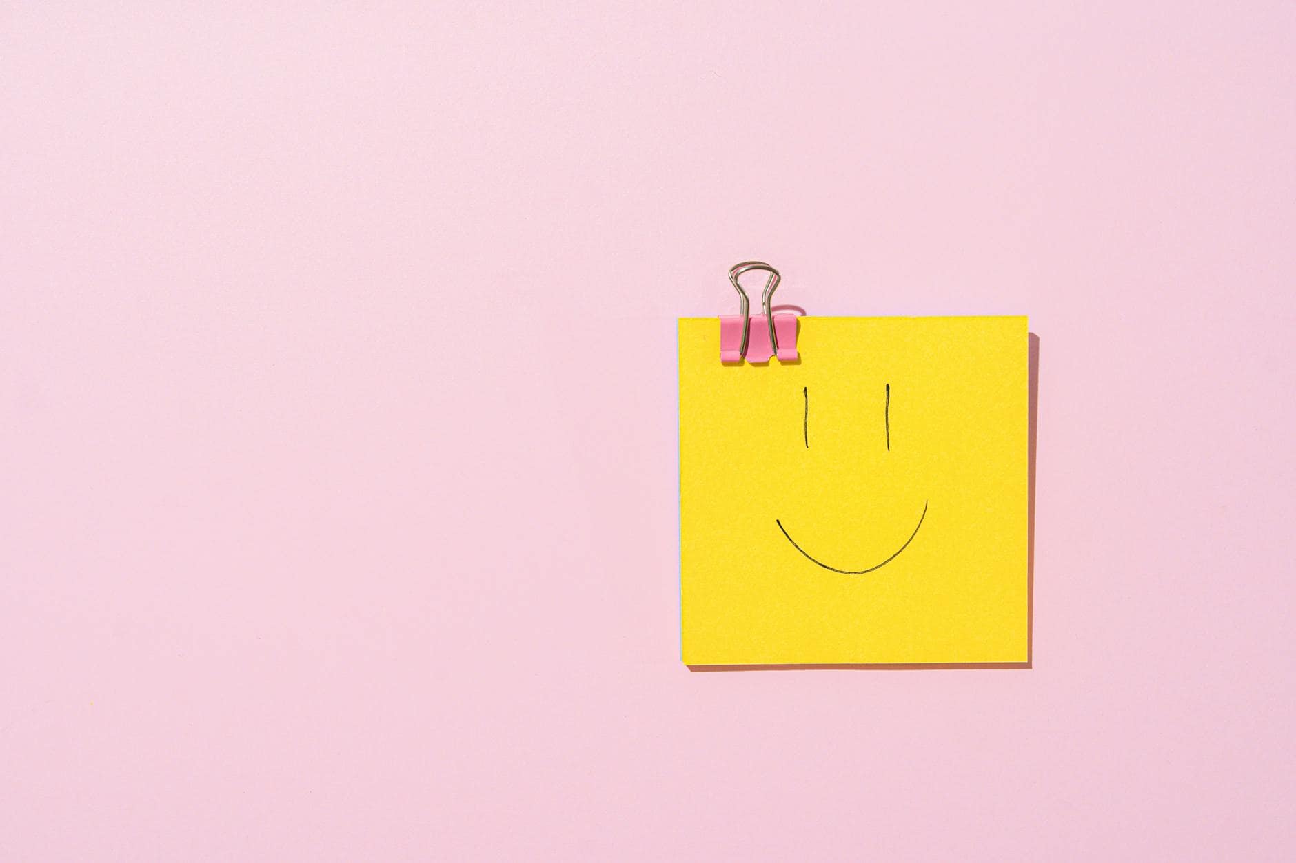 a sticky note with a binder clip on a pink surface