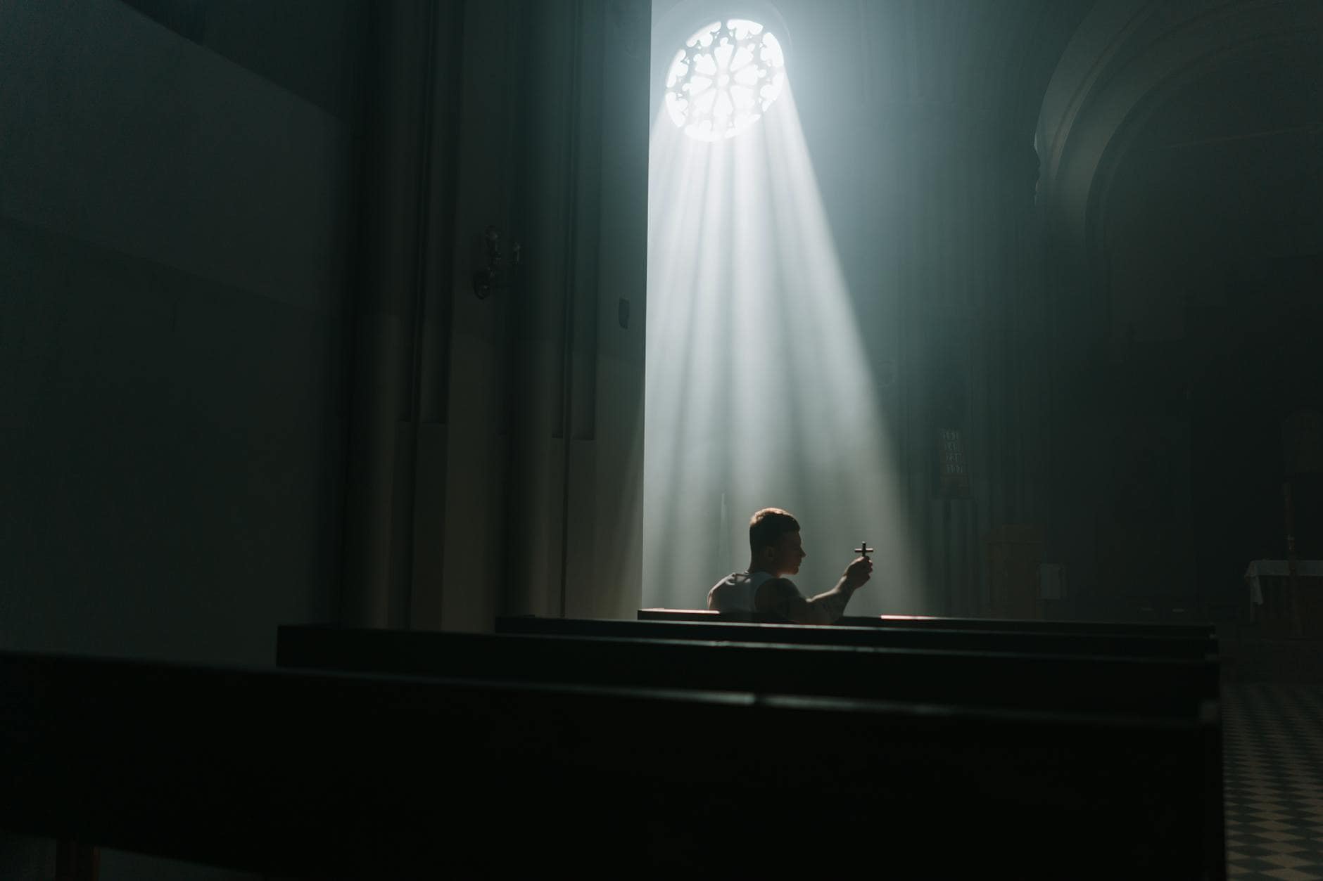man sitting on a pew holding a cross