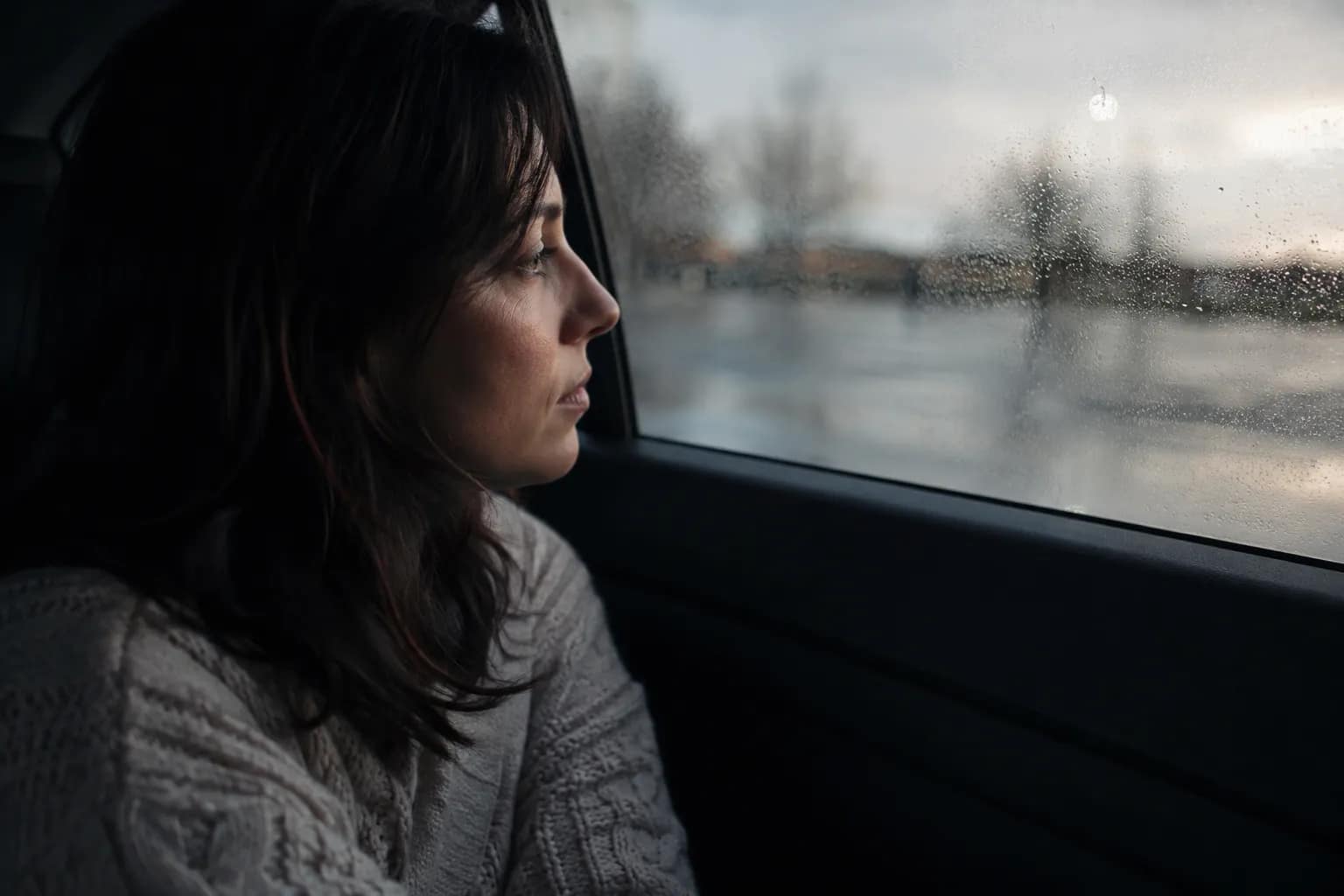 "Woman sitting alone in a car looking out the window in quiet reflection"