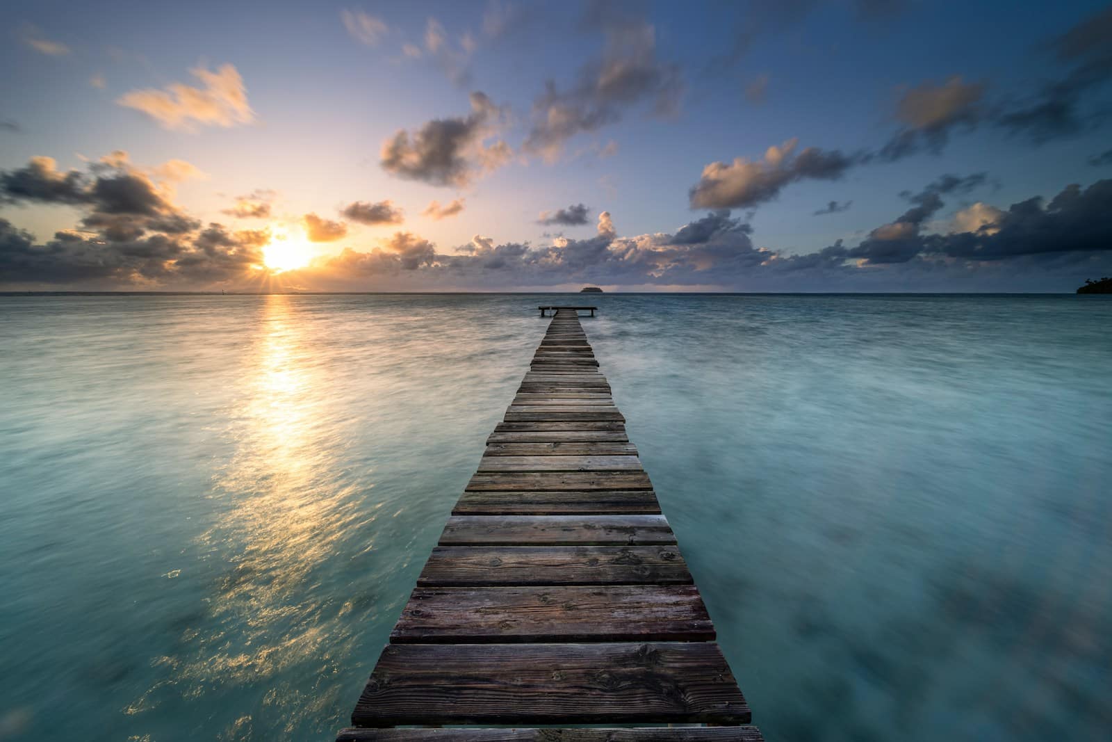 a wooden pier extending into the ocean at sunset