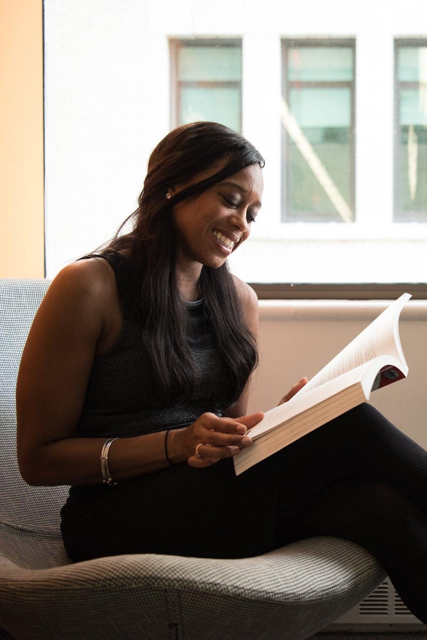 woman in black sleeveless top sitting on gray chair while reading book